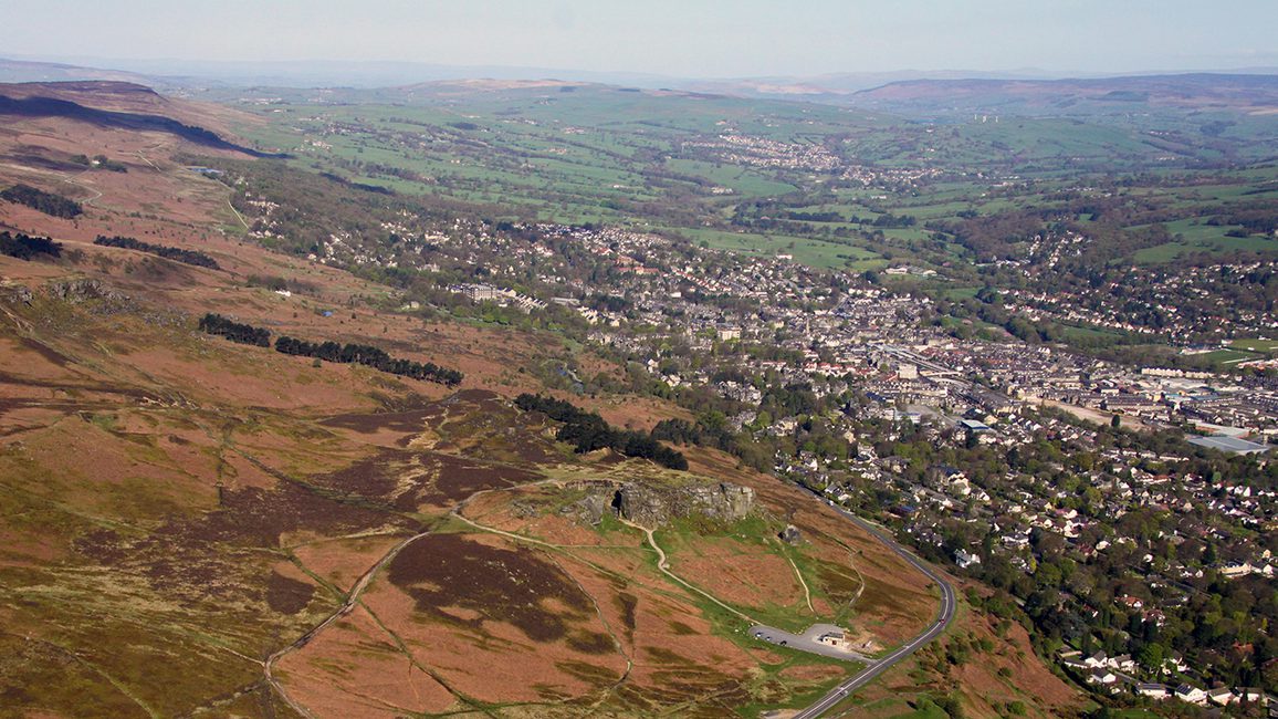 A wide-frame drone shot of The Cow and Calf Rocks, Ilkley Moor in Yorkshire. The image shows hills, fields as well as the town of Ilkley in the distance