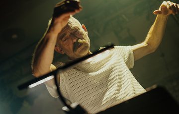 Charles Hazlewood, a man in his fifties with grey hair, a moustache, and light skin tone conducts in front of a music stand.
