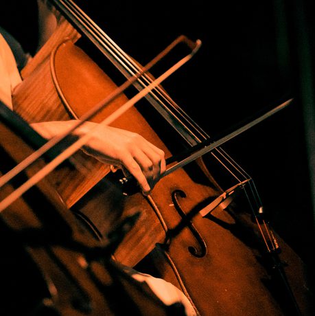 A close-up image of two cellists performing. You can see only the musicians' hands as they bow their instruments.