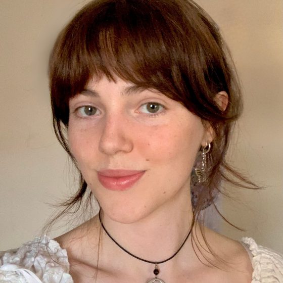 Lauren Edwards, a woman with light skin tone and dark brown hair wearing a white top is looking at the camera and smiling warmly.